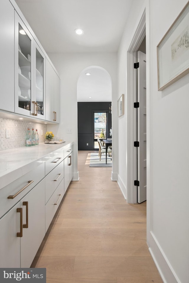 hallway featuring arched walkways, light wood-type flooring, baseboards, and recessed lighting