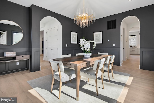 dining area featuring arched walkways, a notable chandelier, visible vents, light wood-style floors, and wainscoting