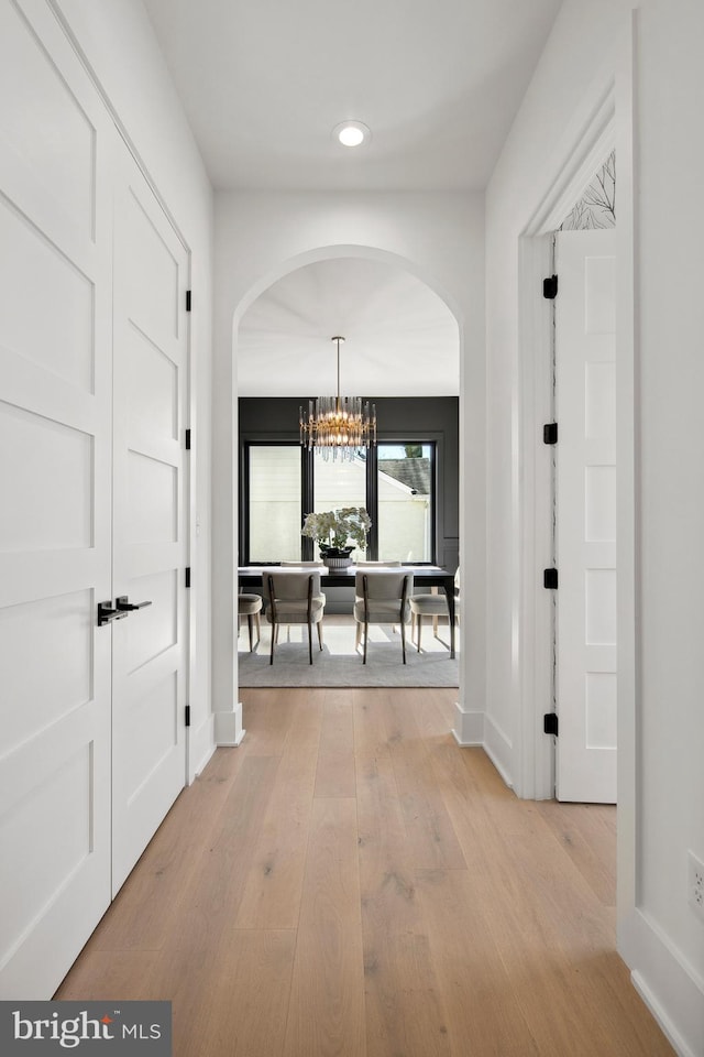 hallway featuring baseboards, arched walkways, light wood-type flooring, a notable chandelier, and recessed lighting