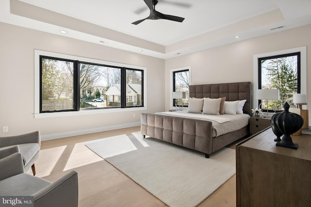 bedroom with light wood finished floors, visible vents, multiple windows, and a tray ceiling