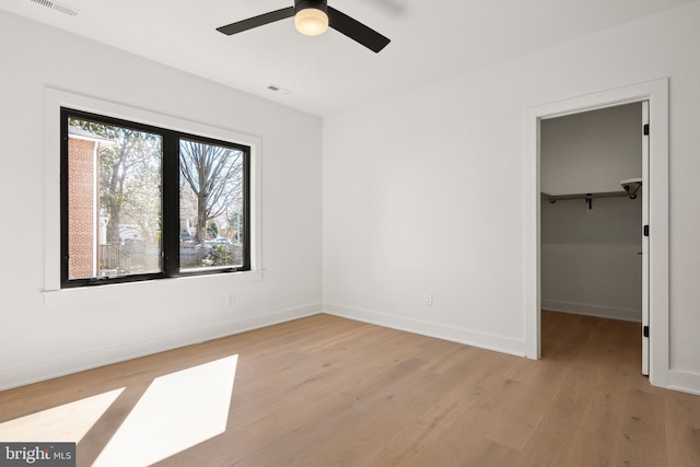 unfurnished bedroom featuring light wood finished floors, baseboards, ceiling fan, a spacious closet, and a closet