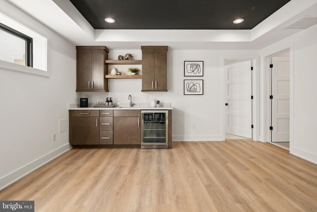 bar with beverage cooler, wet bar, a tray ceiling, and light wood-style flooring