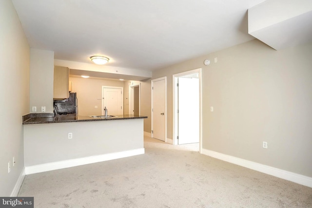 kitchen featuring light colored carpet, a peninsula, a sink, baseboards, and freestanding refrigerator