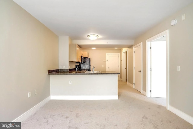 kitchen featuring light carpet, a sink, a peninsula, and baseboards