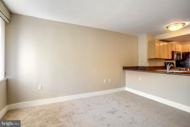 kitchen with light brown cabinets, carpet flooring, a sink, and baseboards