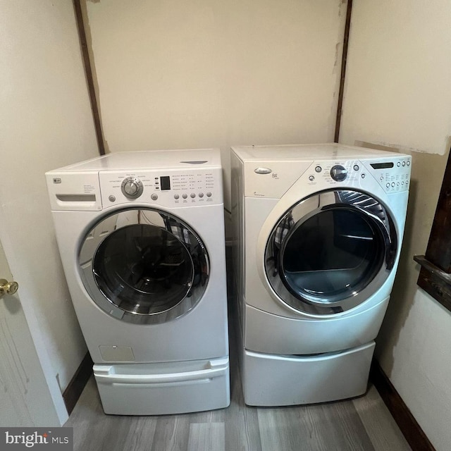 laundry area featuring laundry area, wood finished floors, washing machine and clothes dryer, and baseboards