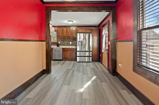 kitchen featuring light wood-style flooring, baseboards, appliances with stainless steel finishes, backsplash, and brown cabinetry