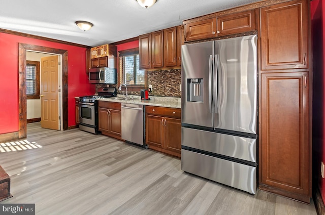 kitchen with light wood-style flooring, stainless steel appliances, a sink, decorative backsplash, and brown cabinetry