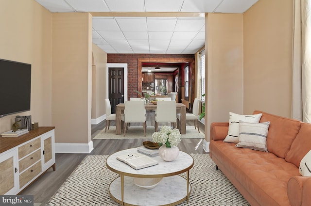 living area with dark wood finished floors, a paneled ceiling, and baseboards