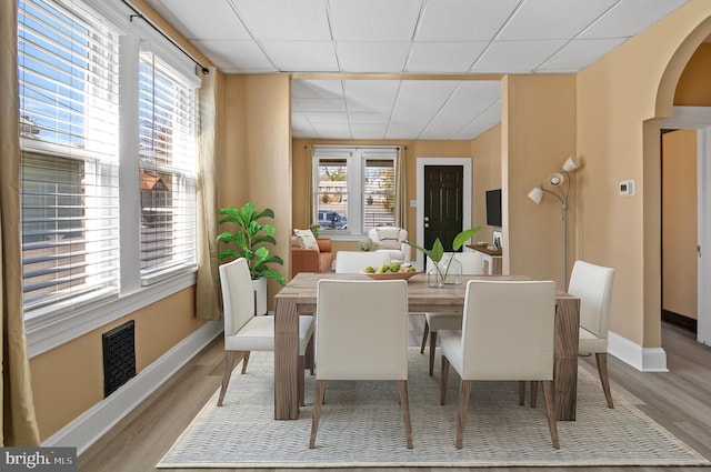 dining room featuring baseboards, a paneled ceiling, visible vents, and light wood-style floors