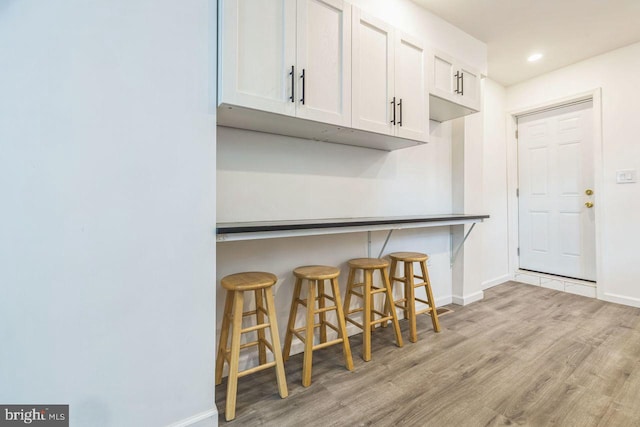 kitchen with recessed lighting, white cabinetry, baseboards, light wood-type flooring, and a kitchen bar