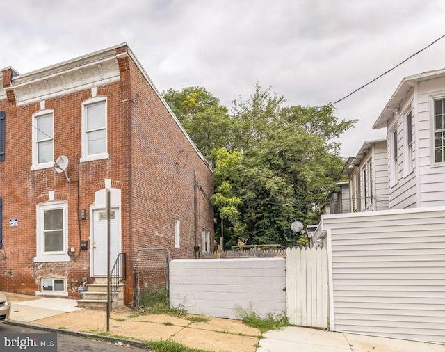 view of side of home featuring entry steps, brick siding, and fence