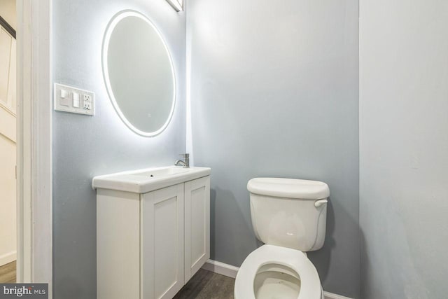 bathroom featuring toilet, baseboards, wood finished floors, and vanity