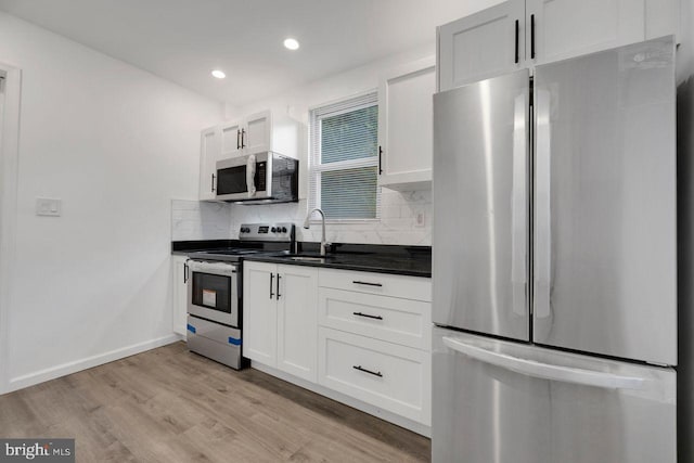 kitchen with a sink, light wood-style floors, appliances with stainless steel finishes, tasteful backsplash, and dark countertops