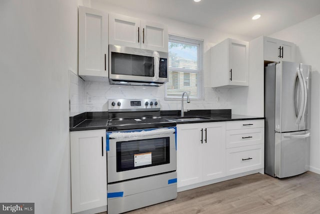 kitchen with tasteful backsplash, dark countertops, appliances with stainless steel finishes, light wood-type flooring, and a sink