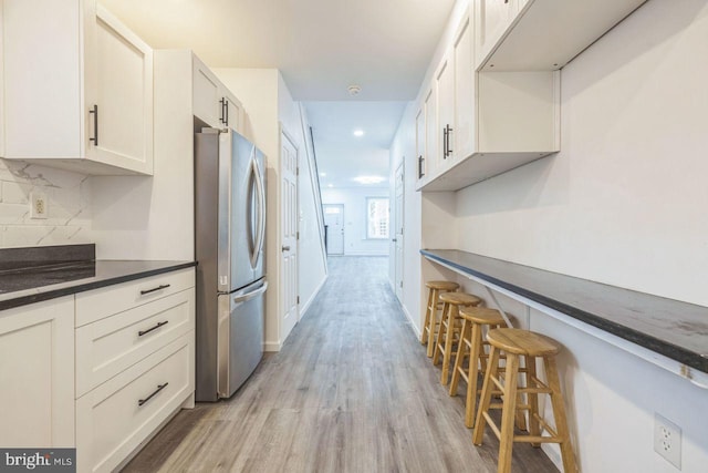 kitchen with dark countertops, backsplash, light wood-style floors, freestanding refrigerator, and a kitchen breakfast bar