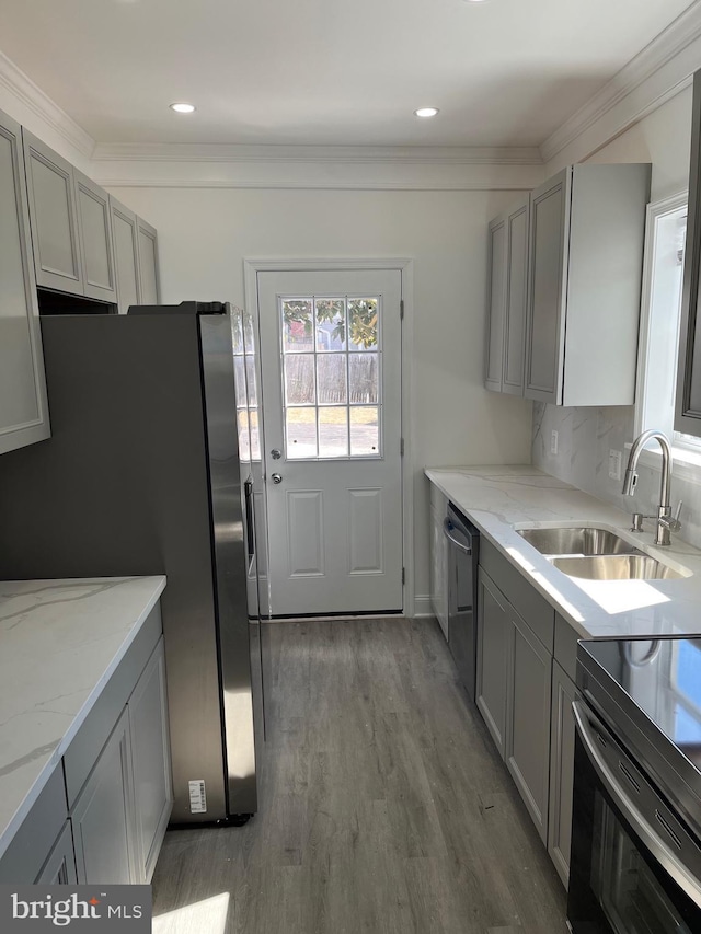 kitchen with light stone counters, stainless steel appliances, wood finished floors, a sink, and gray cabinets