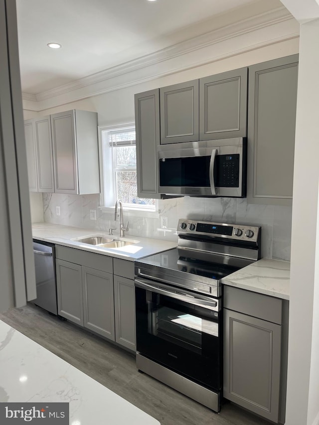 kitchen featuring stainless steel appliances, gray cabinets, decorative backsplash, ornamental molding, and a sink