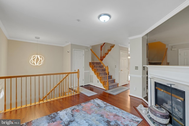 living area with a glass covered fireplace, wood finished floors, stairs, crown molding, and a chandelier