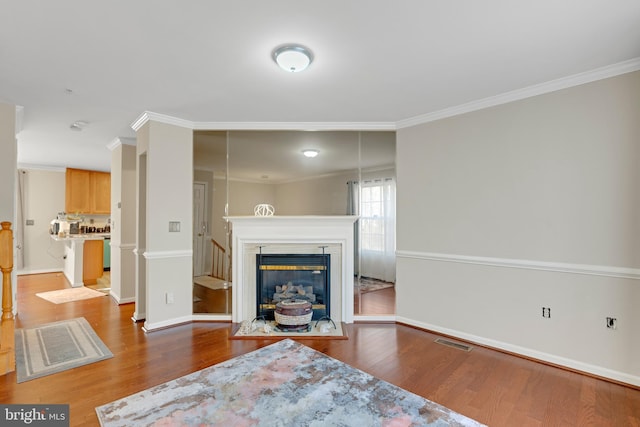 unfurnished living room with wood finished floors, visible vents, baseboards, ornamental molding, and a glass covered fireplace