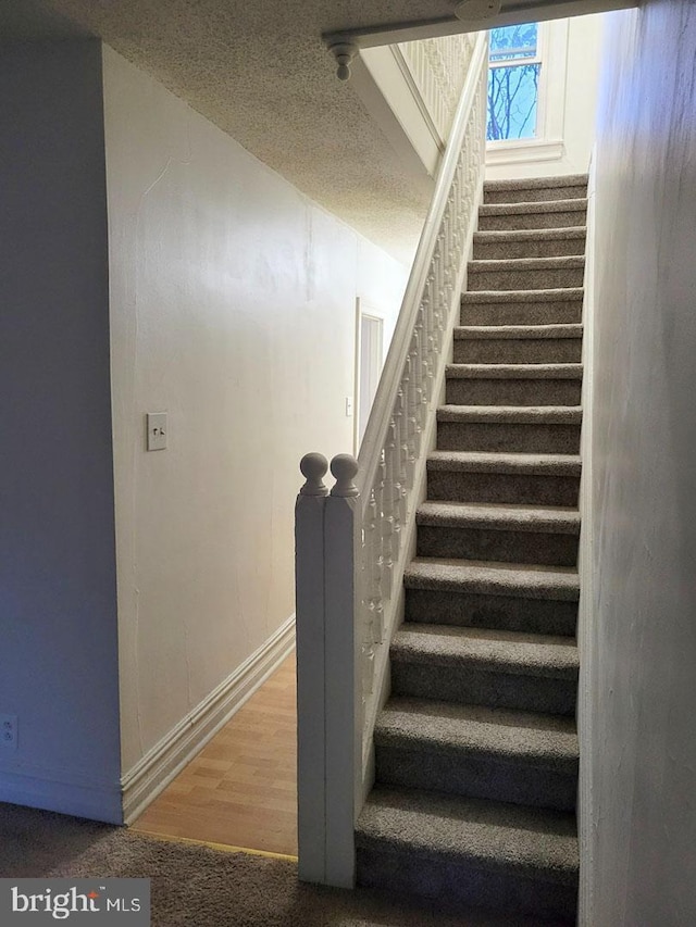 stairway with baseboards, a textured ceiling, and wood finished floors