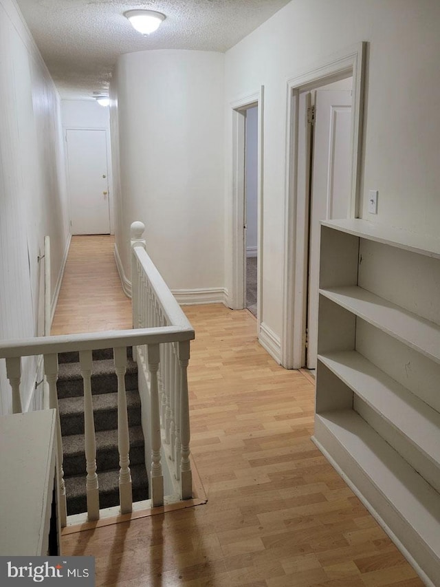 corridor featuring light wood-style floors and a textured ceiling