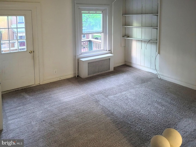 carpeted empty room featuring baseboards and radiator heating unit