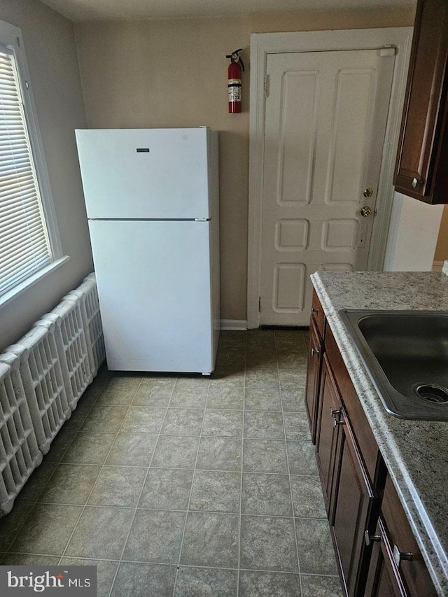 kitchen with radiator heating unit, a sink, freestanding refrigerator, and light stone countertops