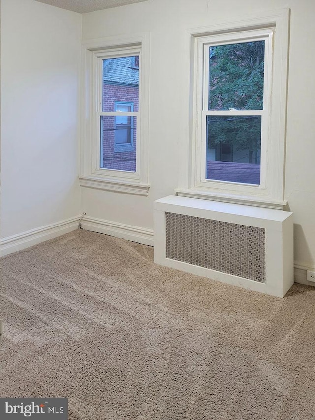 empty room featuring baseboards, carpet flooring, and radiator heating unit