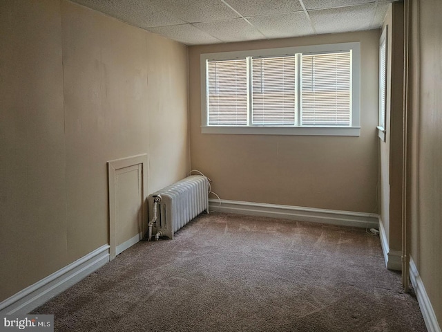 carpeted empty room featuring a paneled ceiling, radiator heating unit, and baseboards