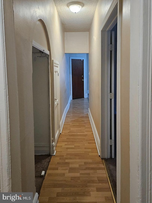 corridor with a textured ceiling, baseboards, and wood finished floors