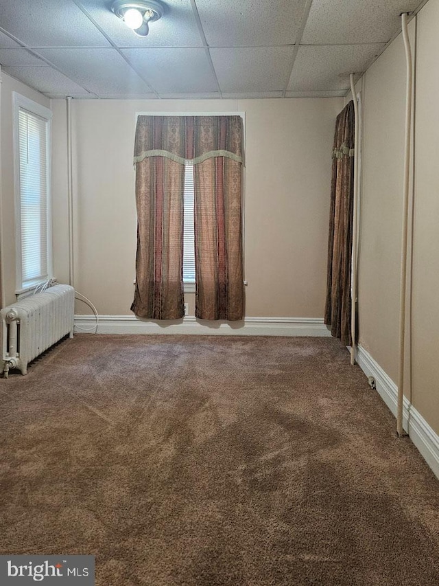 empty room with radiator, baseboards, a drop ceiling, and carpet flooring