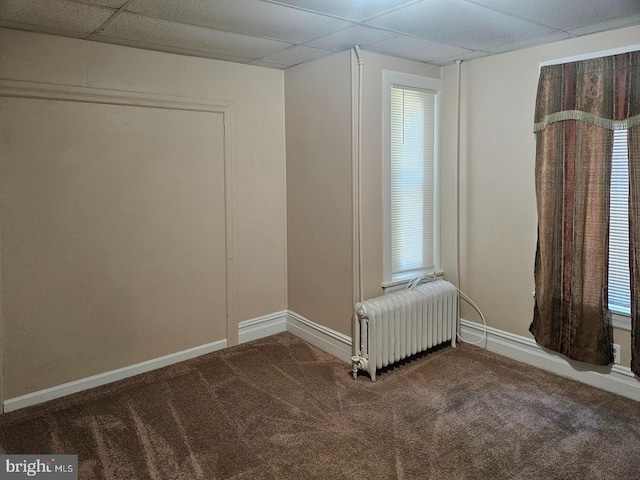 carpeted spare room featuring baseboards, a drop ceiling, and radiator