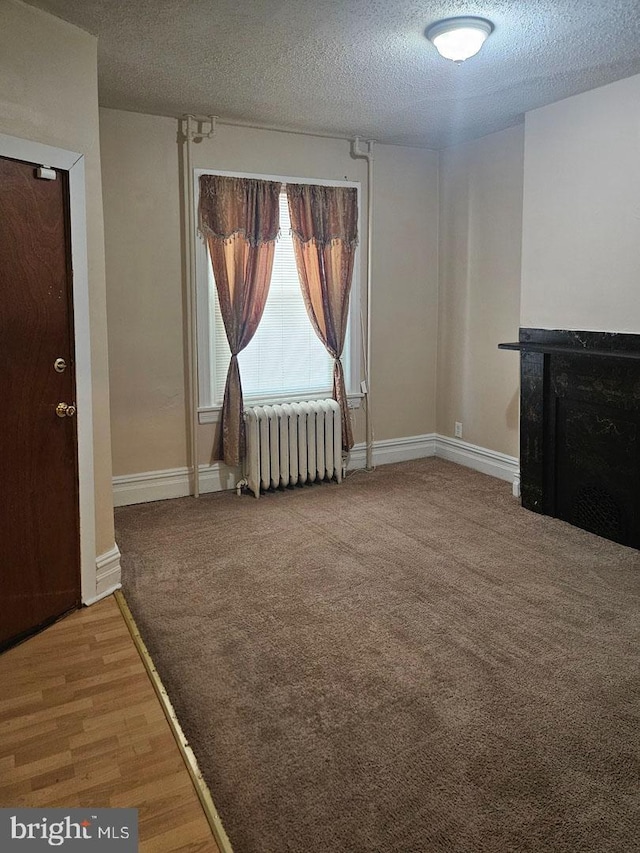 unfurnished living room with radiator, baseboards, a textured ceiling, and carpet flooring