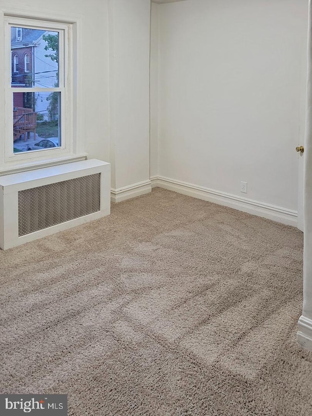 spare room featuring carpet floors, radiator heating unit, and baseboards