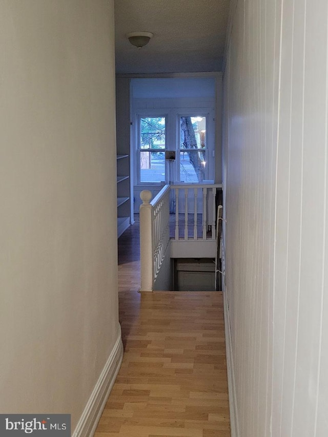 corridor with light wood-style flooring, baseboards, and an upstairs landing