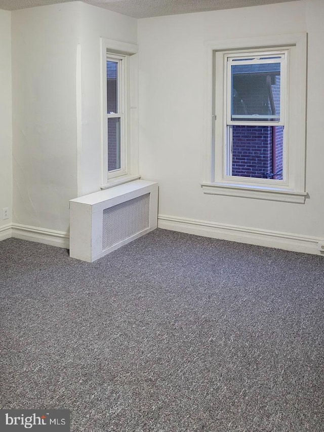 carpeted empty room featuring radiator heating unit, baseboards, and a textured ceiling