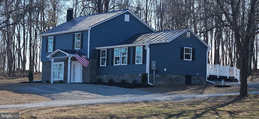 view of front of house with driveway, metal roof, a standing seam roof, and a chimney