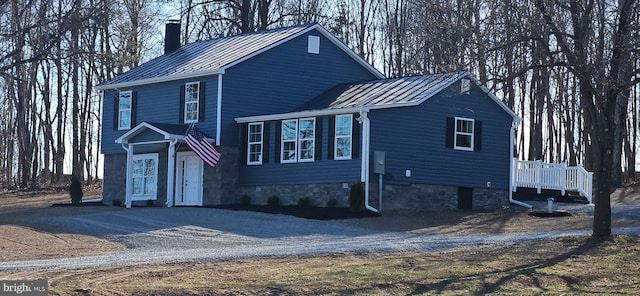 view of front of property with a standing seam roof, a chimney, driveway, and metal roof