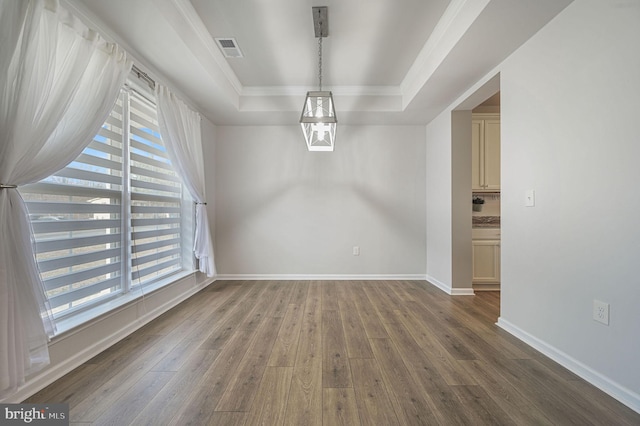 unfurnished dining area featuring hardwood / wood-style floors, baseboards, visible vents, a tray ceiling, and crown molding