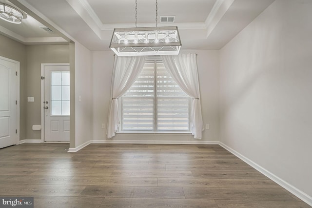 unfurnished dining area with visible vents, a raised ceiling, and wood finished floors