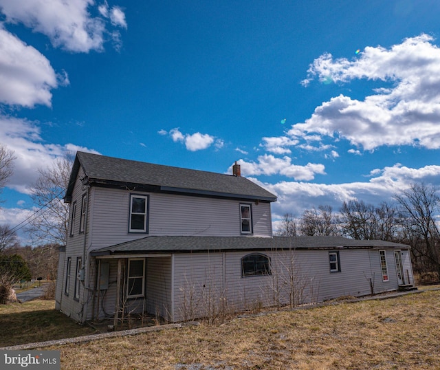 rear view of property featuring a chimney, a lawn, and roof with shingles