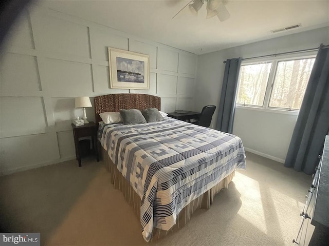 bedroom with a decorative wall, light carpet, a ceiling fan, baseboards, and visible vents