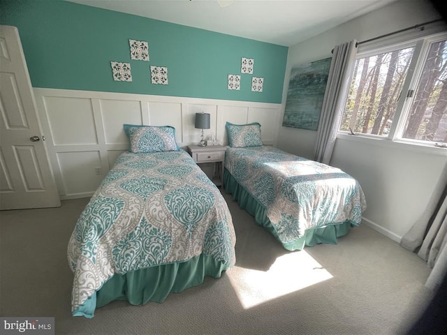 carpeted bedroom featuring a decorative wall and wainscoting