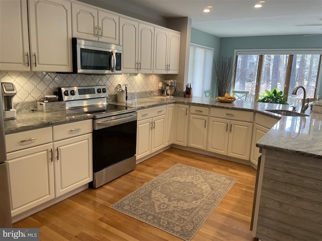 kitchen featuring stainless steel appliances, white cabinets, a sink, and light wood-style flooring