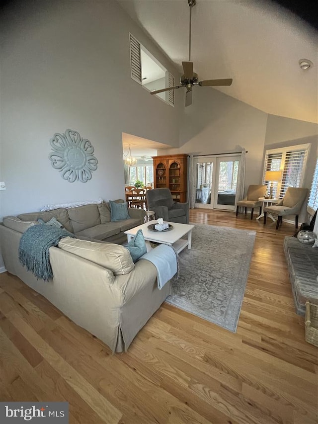 living area featuring light wood-style floors, high vaulted ceiling, a wealth of natural light, and ceiling fan with notable chandelier