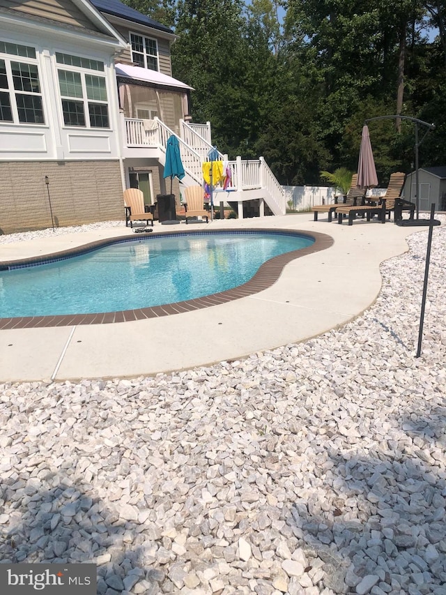 outdoor pool featuring an outbuilding, a deck, a patio, stairway, and a storage shed