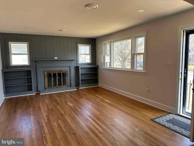 unfurnished living room with a glass covered fireplace, baseboards, and wood finished floors