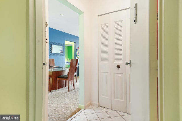 hall featuring light carpet, baseboards, and light tile patterned flooring