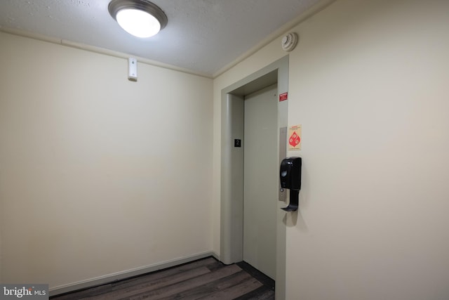 hallway featuring dark wood-style flooring, elevator, and baseboards